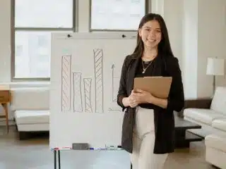 Woman in Black Blazer Standing Beside a Whiteboard with Graphs